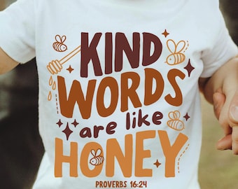 Puede incluir: Camiseta blanca para niños pequeños con el texto "KIND WORDS are like HONEY" en marrón y naranja. La camiseta presenta gráficos relacionados con abejas y miel y el versículo bíblico Proverbios 16:24.