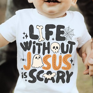May include: A white short-sleeved t-shirt featuring the black and orange text "LIFE WITHOUT JESUS IS SCARY" with graphic illustrations of a bone, a spider web, a skull, a ghost, a spider, and a bat integrated into the lettering design.
