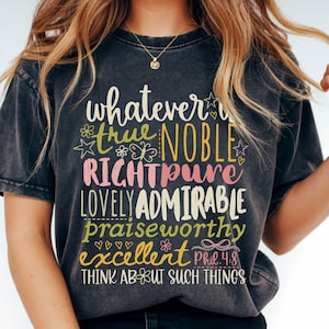 May include: Dark gray t-shirt with the words "whatever is true, noble, right, pure, lovely, admirable, praiseworthy, excellent" in a colorful, whimsical font. The text is accompanied by floral and heart graphics. The shirt also includes the text "Think about such things".