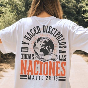 May include: White t-shirt with a graphic on the back. The design features a hand holding a globe, with Spanish text around it. The text reads "ID Y HACED DISCIPULOS A TODAS LAS NACIONES MATEO 28:19".