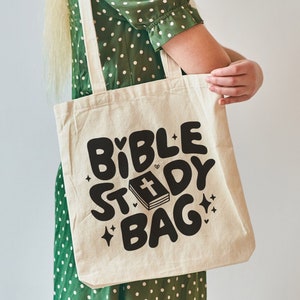 May include: A white canvas tote bag with black text that reads "Bible Study Bag" and a stylized image of a closed book with a cross on the cover.