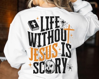 Könnte beinhalten: Weißes Sweatshirt mit einem Aufdruck auf der Rückseite. Das Design zeigt ein Kreuz, eine Bibel, einen Kürbis und Spinnen, mit dem Text "LIFE WITHOUT JESUS IS SCORY" in Schwarz und Orange.
