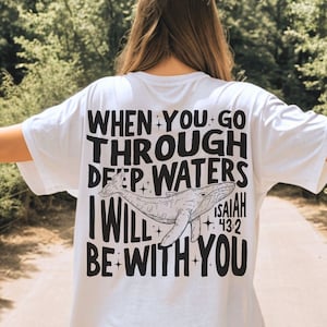 May include: White t-shirt with a black graphic print of a whale and the text "WHEN YOU GO THROUGH DEEP WATERS I WILL BE WITH YOU" and "ISAIAH 43:2".