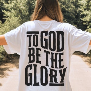 May include: White t-shirt with black text on the back that reads "To God Be The Glory".