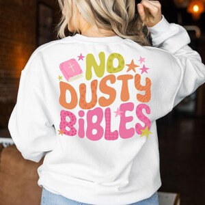 May include: White sweatshirt with the text "NO DUSTY BIBLES" in a retro font. The design includes a pink book, stars, and a mix of orange, green, and pink colors. A casual, comfortable top.
