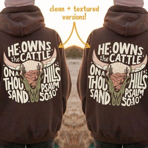 May include: A brown hoodie with a graphic on the back that reads "He Owns the Cattle On a Thousand Hills Psalm 50:10". The graphic features a bull skull, desert landscape, and cactus.
