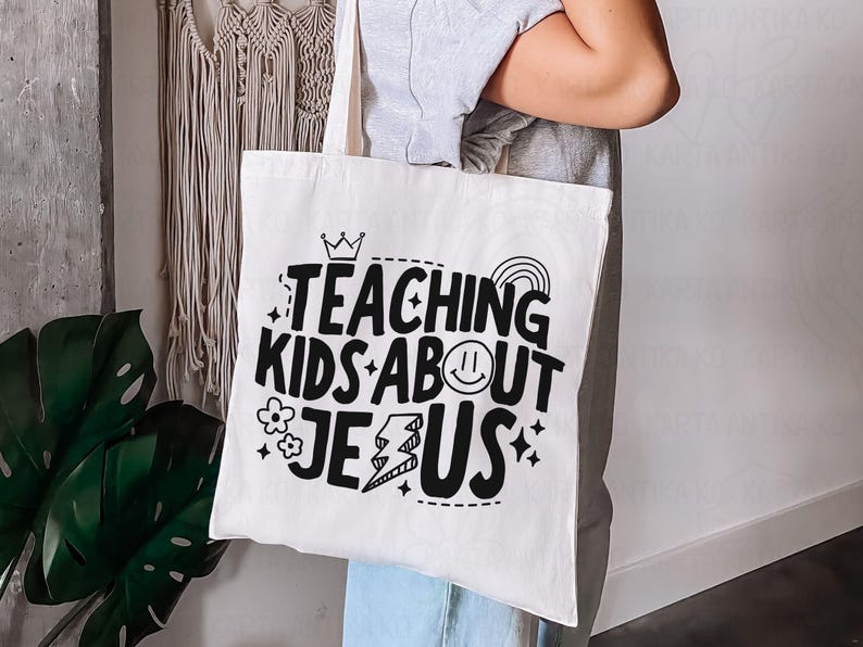 Puede incluir: Un bolso de mano blanco con el texto "TEACHING KIDS ABOUT JESUS" en negro, con una corona, un arco&iacute;ris, una carita sonriente, una flor y gr&aacute;ficos de rel&aacute;mpagos. El bolso lo sostiene una persona.