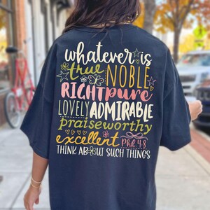 May include: Navy blue t-shirt with colorful text on the back. The text includes words like "true," "noble," and "admirable," along with the phrase "Think about such things." The design features floral and star accents.
