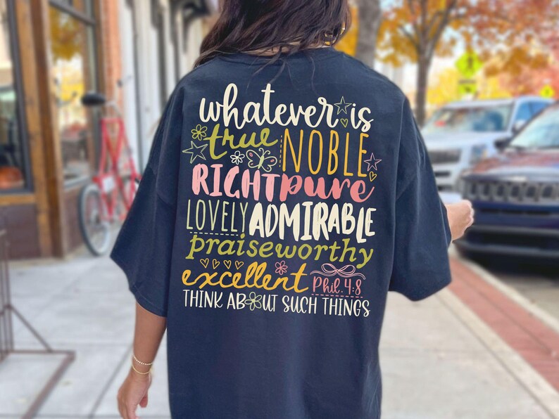 May include: Navy blue t-shirt with colorful text on the back. The text includes words like "true," "noble," and "admirable," along with the phrase "Think about such things." The design features floral and star accents.