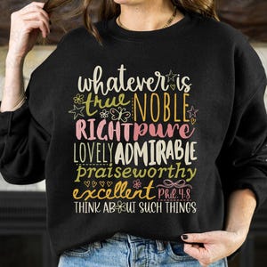 May include: Black sweatshirt with colorful text that reads "whatever is true, noble, right, pure, lovely, admirable, praiseworthy, excellent." The text is in various fonts and colors, with floral and star accents. The phrase "Think about such things" is at the bottom.