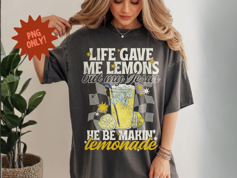 May include: Dark gray t-shirt with the text "LIFE GAVE ME LEMONS but my Jesus HE BE MAKIN' lemonade." The graphic includes a glass of lemonade, lemons, and star accents. The shirt is a vintage style.