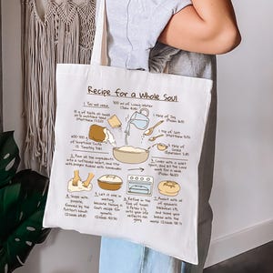 May include: White tote bag with a recipe illustration titled "Recipe for a Whole Soul." The recipe includes ingredients like living water, faith, and grace. The bag is held by a person.