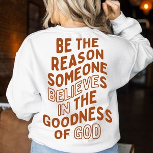 Może przedstawiać: Biała bluza z napisem "BE THE REASON SOMEONE BELIEVES IN THE GOODNESS OF GOD" w brązowych literach.