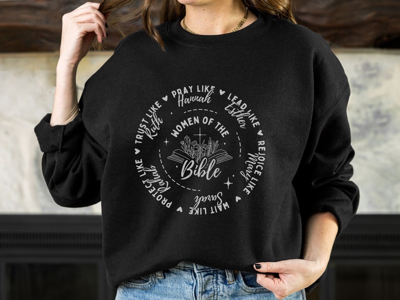 May include: Black sweatshirt with a white graphic design featuring a circle with the words "Women of the Bible" and a Bible with flowers. The circle is surrounded by phrases like "Trust like Ruth", "Pray like Hannah", "Lead like Esther", "Rejoice like Mary", "Wait like Sarah", "Protect like Ruth", and "Serve like Mary".