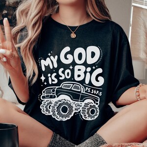 Puede incluir: Camiseta negra con un gr&aacute;fico blanco de un cami&oacute;n monstruo y el texto "My God is so Big" con la referencia b&iacute;blica "PS. 147:5".