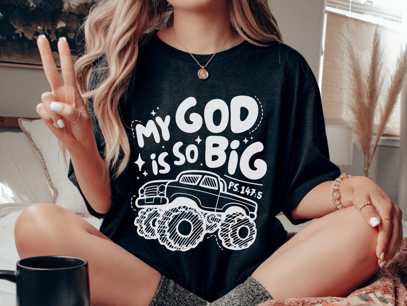 Puede incluir: Camiseta negra con un gr&aacute;fico blanco de un cami&oacute;n monstruo y el texto "My God is so Big" con la referencia b&iacute;blica "PS. 147:5".