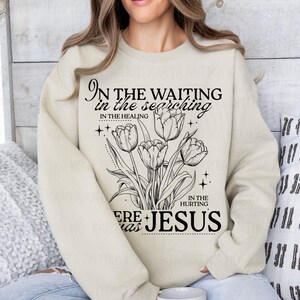 May include: Cream-colored sweatshirt featuring a black floral design with tulips and the text "In the waiting, in the searching, in the healing, in the hurting, here was Jesus." The design includes stars and decorative elements.