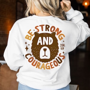 May include: White sweatshirt with a brown bear graphic and the text "Be Strong and Courageous Jsh. 1:9".