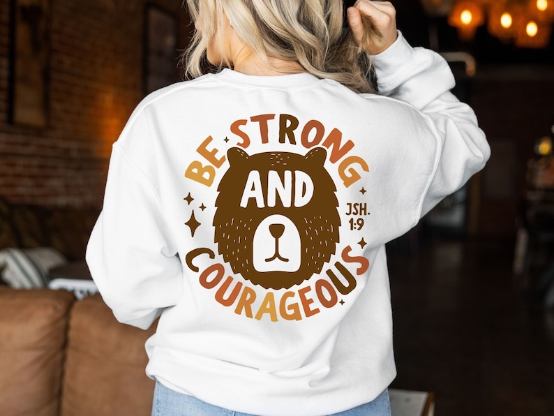 May include: White sweatshirt with a brown bear graphic and the text "Be Strong and Courageous Jsh. 1:9".