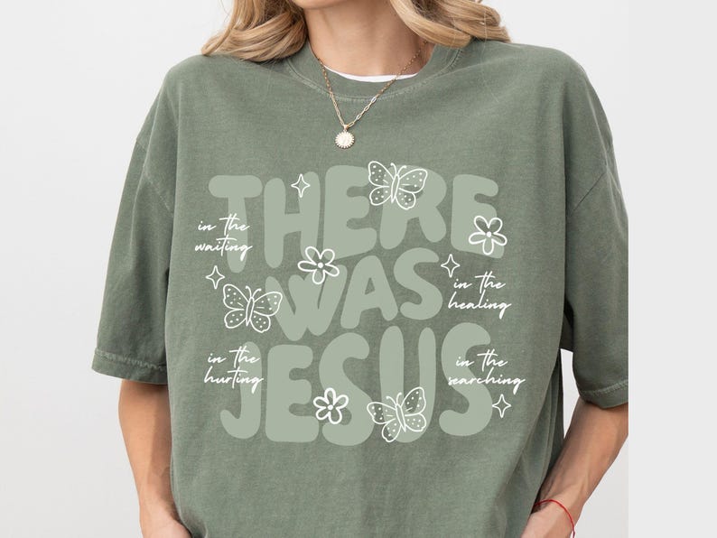 May include: Sage green t-shirt with the text "THERE WAS JESUS" in a rounded font. The design includes white butterflies, flowers, and stars. Additional text reads "in the waiting, in the hurting, in the healing, in the searching."