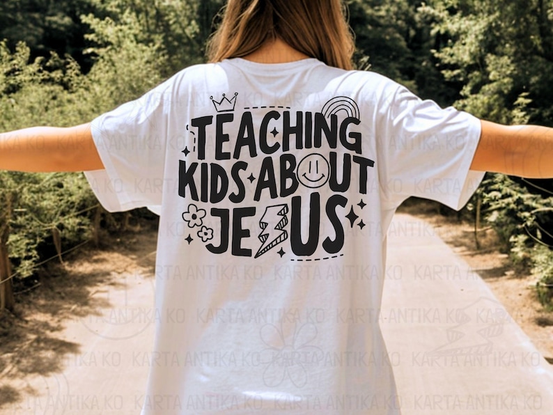 Puede incluir: Camiseta blanca con la frase negra "TEACHING KIDS ABOUT JESUS". El dise&ntilde;o incluye una corona, un arco&iacute;ris, una carita sonriente, flores, un rayo y estrellas. Una camiseta informal.