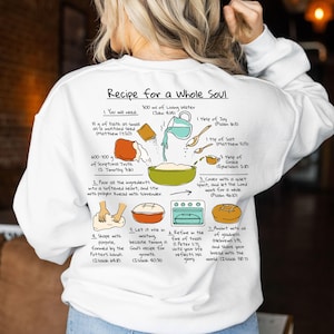 May include: White long-sleeve sweatshirt with a graphic on the back that reads "Recipe for a Whole Soul." The graphic is a diagram with instructions and ingredients for making bread, including text from the Bible.