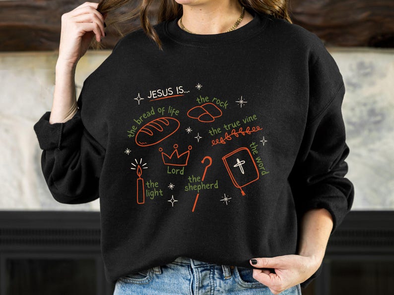 May include: Black sweatshirt with a white graphic design that says "JESUS IS..." and lists several attributes of Jesus, including "the bread of life", "the rock", "the true vine", "the light", "the Lord", "the shepherd", and "the word".