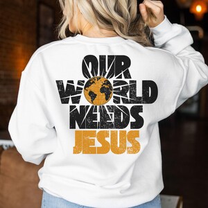 May include: White sweatshirt with the text "OUR WORLD NEEDS JESUS" in black and orange. The design includes a globe graphic. The sweatshirt is a casual, long-sleeved garment.