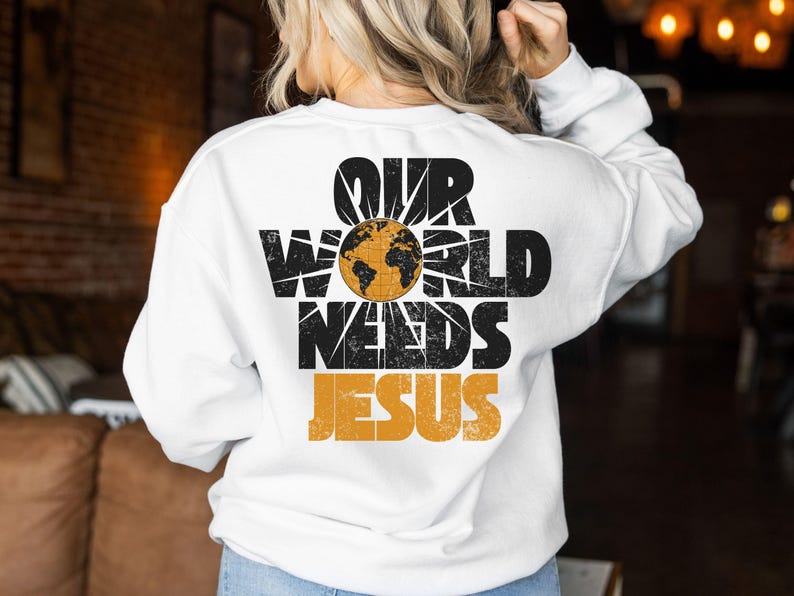 May include: White sweatshirt with the text "OUR WORLD NEEDS JESUS" in black and orange. The design includes a globe graphic. The sweatshirt is a casual, long-sleeved garment.