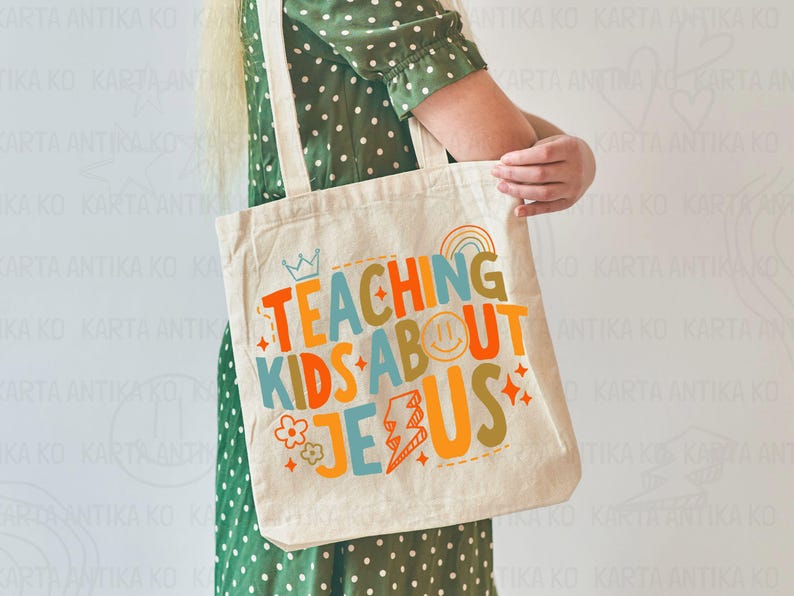 Puede incluir: Bolso tote de color crema con el texto "TEACHING KIDS ABOUT JESUS" en letras coloridas. El dise&ntilde;o incluye una corona, un arco&iacute;ris, una carita sonriente, una flor y un rayo. El bolso tiene dos correas beige.