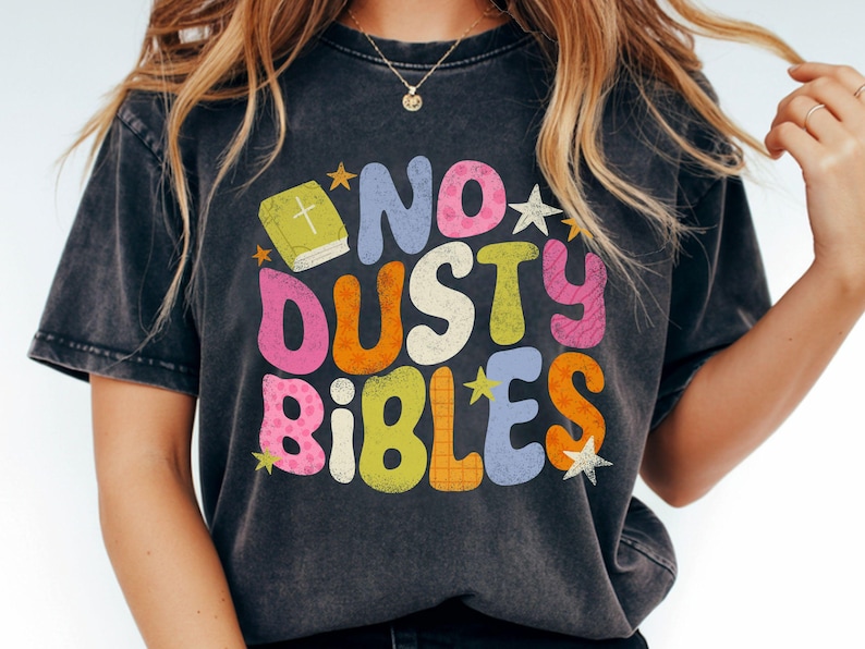 May include: Dark gray t-shirt with the words "NO DUSTY BIBLES" in colorful, retro-style lettering. The design includes a book with a cross and star accents, creating a vintage, inspirational aesthetic.