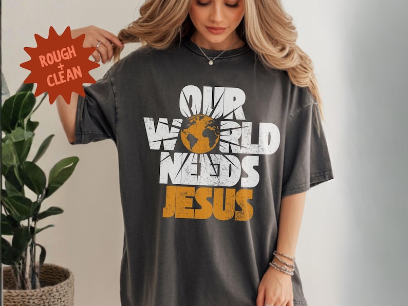 May include: Dark gray t-shirt with the text "OUR WORLD NEEDS JESUS" in white and orange. The design includes a globe and sun graphic. The shirt is a relaxed fit.