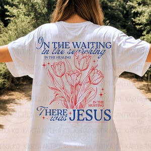 May include: White t-shirt with a floral design of red tulips and the text "In the waiting, in the searching, in the healing, in the hurting, there was Jesus" in blue. The shirt has a relaxed fit.