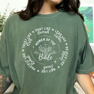 May include: A green t-shirt with a white circle design featuring the text "Women of the Bible" and names of women from the Bible, including Ruth, Hannah, Esther, Mary, and Sarah.