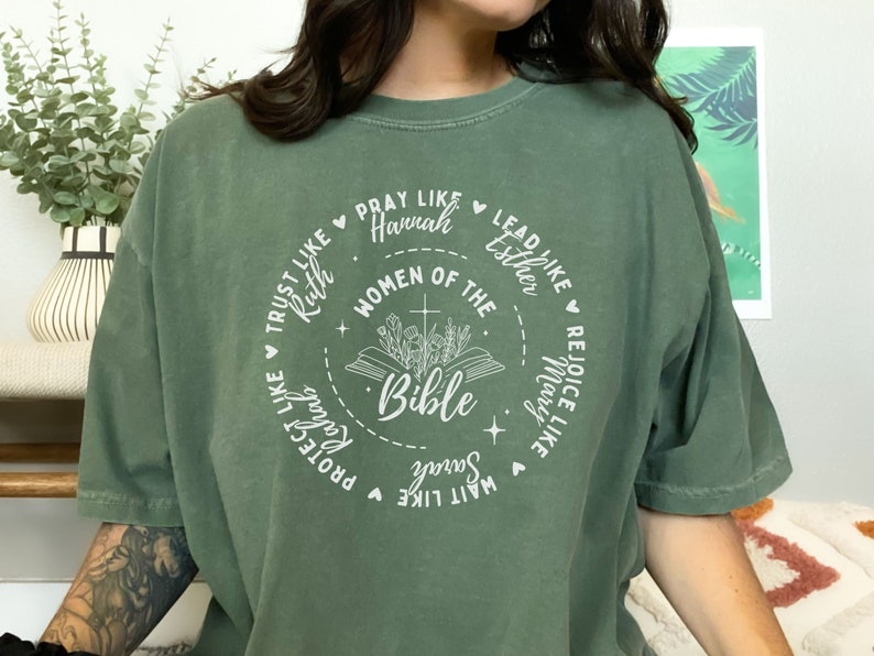 May include: A green t-shirt with a white circle design featuring the text "Women of the Bible" and names of women from the Bible, including Ruth, Hannah, Esther, Mary, and Sarah.