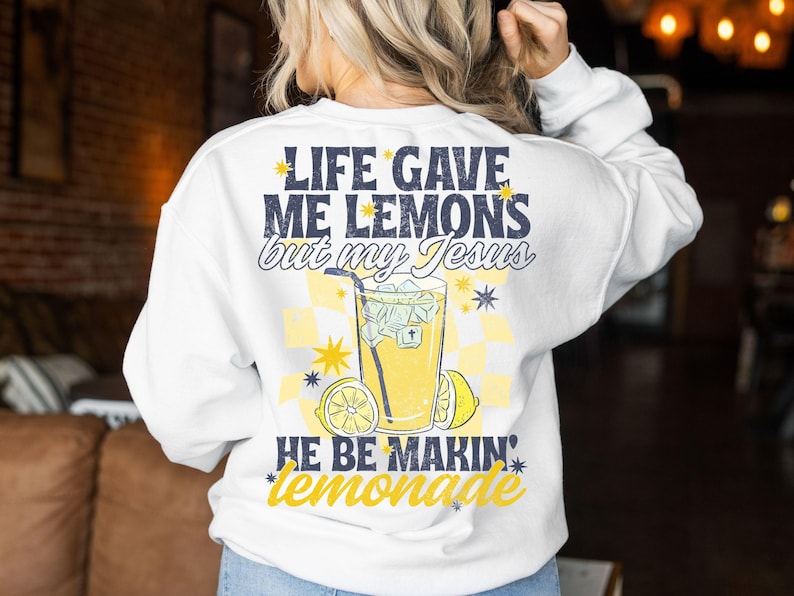 May include: White sweatshirt with a graphic on the back that says "LIFE GAVE ME LEMONS but my Jesus HE BE MAKIN' lemonade." The graphic includes a glass of lemonade, lemons, and stars in yellow and blue.
