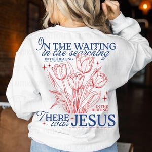 May include: White sweatshirt with a red and blue floral design and text. The text reads "In the waiting, in the searching, in the healing, in the hurting, there was Jesus."