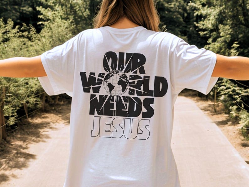 May include: White t-shirt with the text "OUR WORLD NEEDS JESUS" in black, featuring a globe graphic. The shirt is a casual style, suitable for everyday wear.