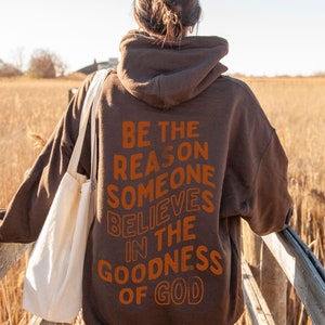 Może przedstawiać: Brązowa bluza z kapturem z nadrukiem "Be the reason someone believes in the goodness of God" na plecach w kolorze pomarańczowym.