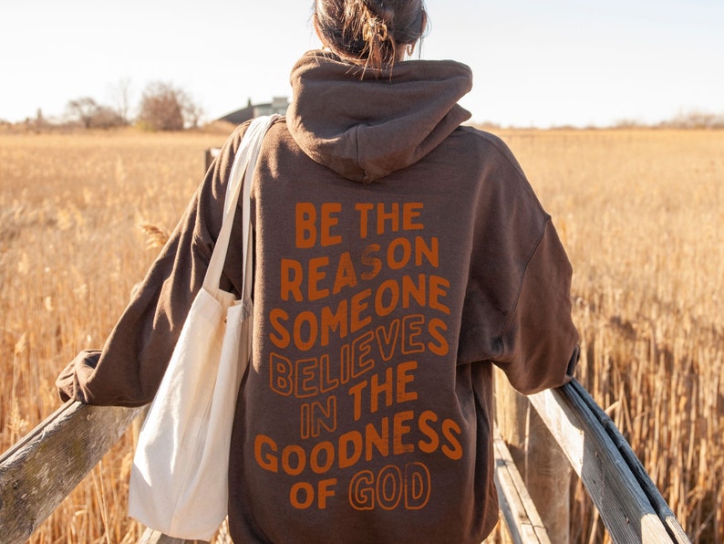 Może przedstawiać: Brązowa bluza z kapturem z nadrukiem "Be the reason someone believes in the goodness of God" na plecach w kolorze pomarańczowym.