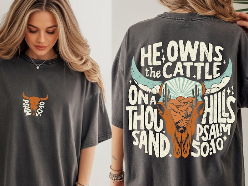 May include: Dark gray t-shirt with a graphic design featuring a bull skull, desert landscape, and the text "He Owns the Cattle on a Thousand Hills Psalm 50:10." A smaller version of the design is on the front.