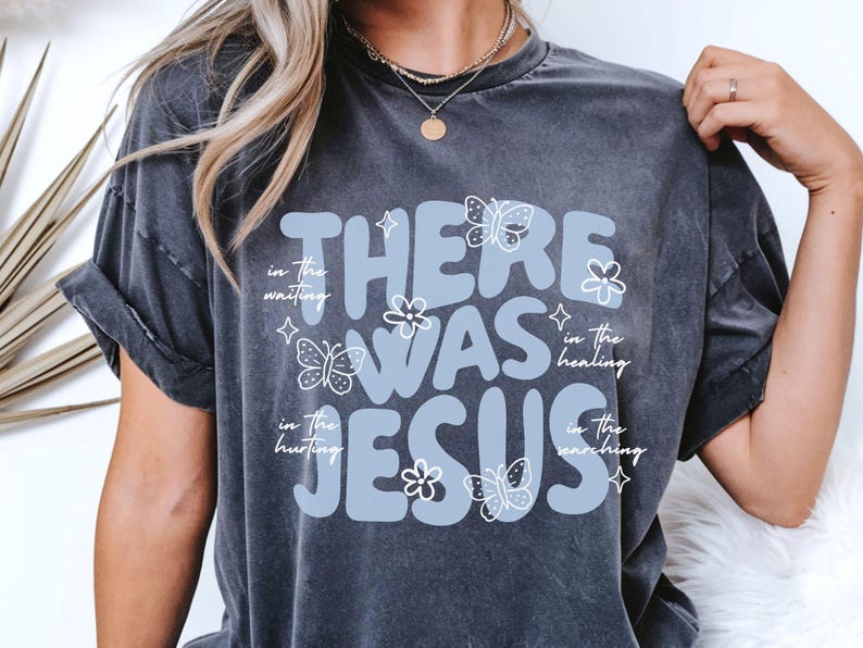 May include: Dark gray t-shirt with the text "THERE WAS JESUS" in light blue, accompanied by butterfly and flower graphics. Additional text includes "in the waiting, in the healing, in the hurting, in the searching."