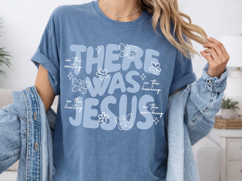 May include: A blue t-shirt with the words "THERE WAS JESUS" in large, light blue letters. The design includes butterflies, flowers, and the phrases "in the waiting," "in the healing," "in the hurting," and "in the searching" in white script.