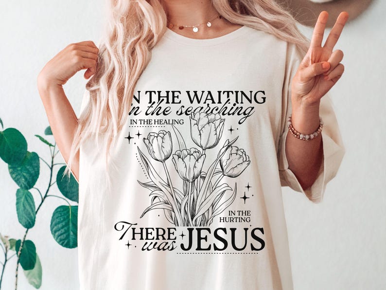 May include: Cream-colored t-shirt featuring a black and white floral design with the words "IN THE WAITING, IN THE SEARCHING, IN THE HEALING, IN THE HURTING, THERE WAS JESUS."