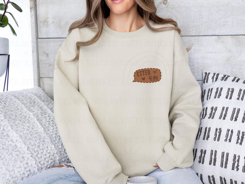 May include: Cream-colored sweatshirt with a brown speech bubble graphic. The speech bubble contains the text "ESTER 4:14" in a handwritten style, with a small heart symbol. The sweatshirt is a casual, long-sleeved garment.