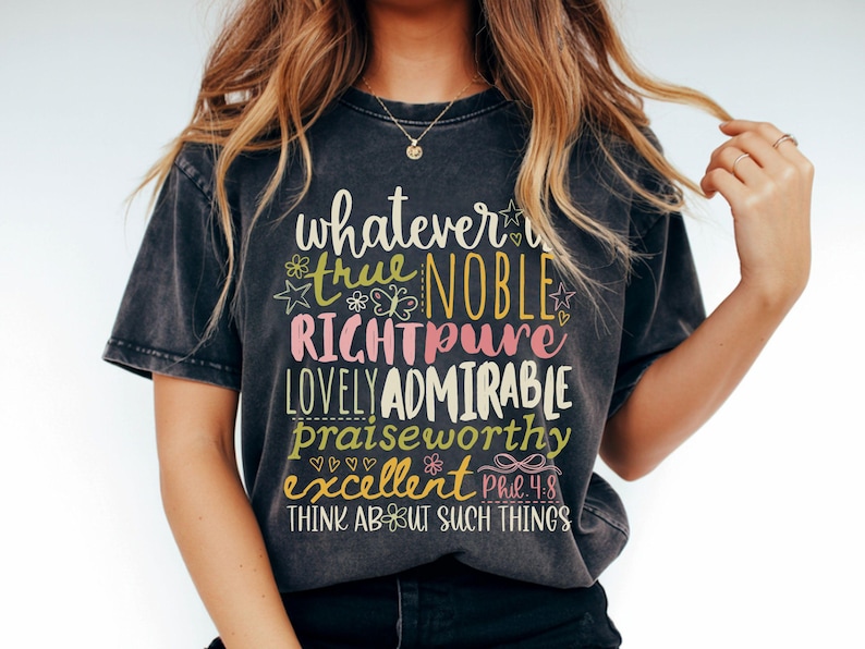 May include: Dark gray t-shirt with the words "whatever is true, noble, right, pure, lovely, admirable, praiseworthy, excellent" in a colorful, whimsical font. The text is accompanied by floral and heart graphics. The shirt also includes the text "Think about such things".