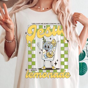 Op de afbeelding: Cr&egrave;mekleurig T-shirt met een retro-stijl afbeelding van een cartoon limonadeglas. De tekst luidt: "Life gave me some lemons, but Jesus he be makin' lemonade".