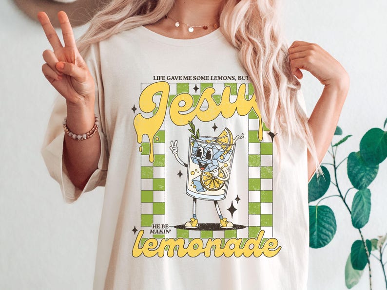 Op de afbeelding: Cr&egrave;mekleurig T-shirt met een retro-stijl afbeelding van een cartoon limonadeglas. De tekst luidt: "Life gave me some lemons, but Jesus he be makin' lemonade".
