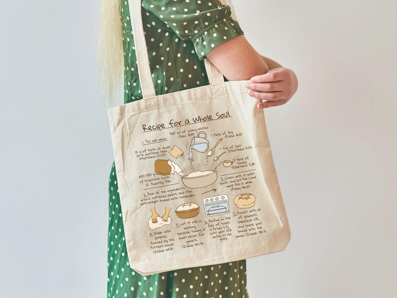 May include: Cream-colored tote bag with the text "Recipe for a Whole Soul" and a recipe illustration. The recipe includes ingredients like faith, joy, and grace. The bag is held by a person wearing a green polka dot dress.