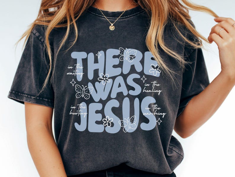 May include: Dark gray t-shirt with the text "THERE WAS JESUS" in light blue, adorned with butterfly and flower graphics. Additional text includes "in the waiting", "in the healing", "in the hurting", and "in the searching".
